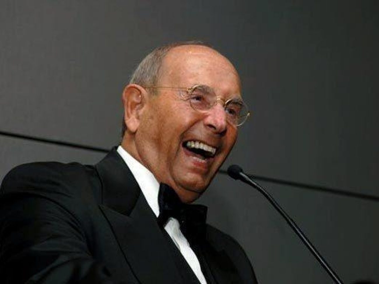 Rich DeVos wearing a tuxedo at a microphone.